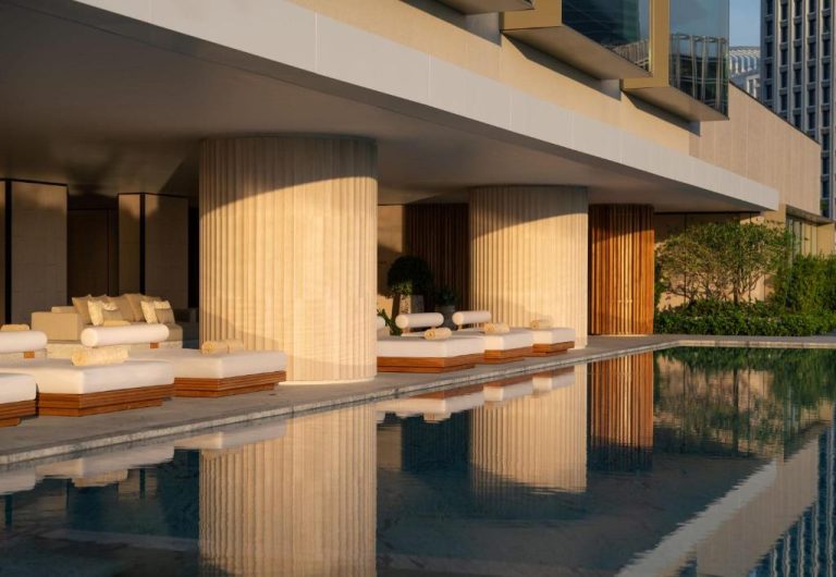 Piscina exterior con tumbonas de lujo y columnas iluminadas al atardecer en el Dusit Thani Bangkok