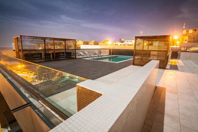 Piscina en terraza rooftop del Hotel Pérola iluminada de noche con pérgolas de madera y vistas a la ciudad