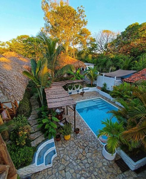 Piscina exterior con jardín tropical y cabañas de paja en Hotel Cabañas Puesta del Sol
