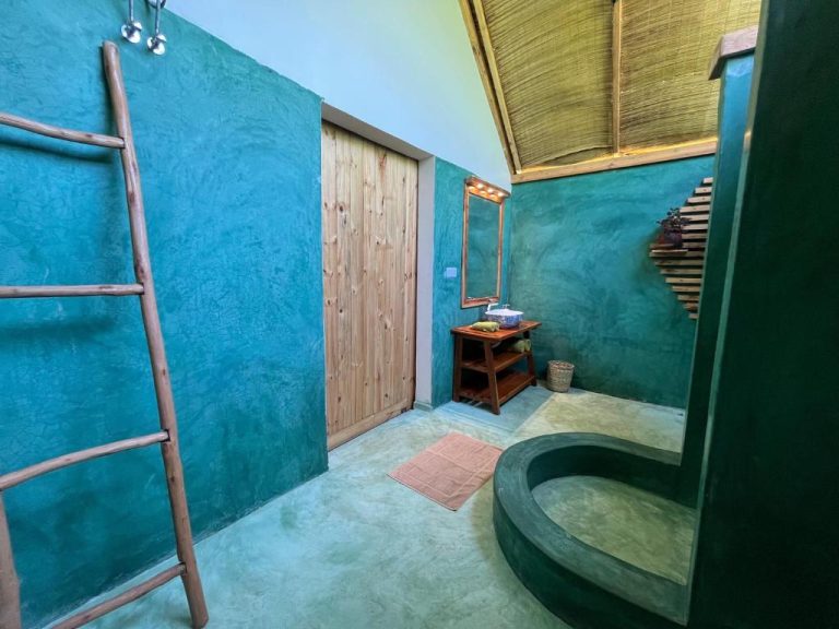 Baño rústico con bañera integrada y paredes turquesa en Kidoti Bay, techo de paja y detalles de bambú