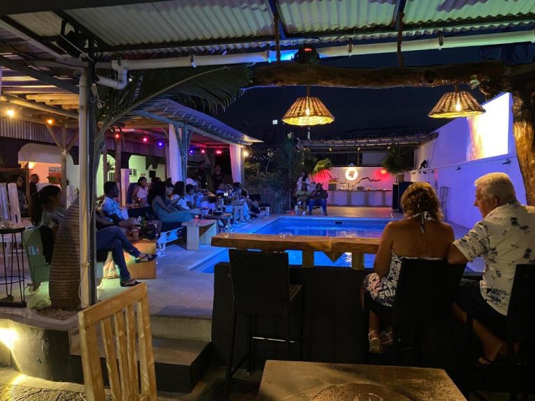 Terraza con piscina iluminada y ambiente nocturno en el hotel Le Pôle con clientes disfrutando