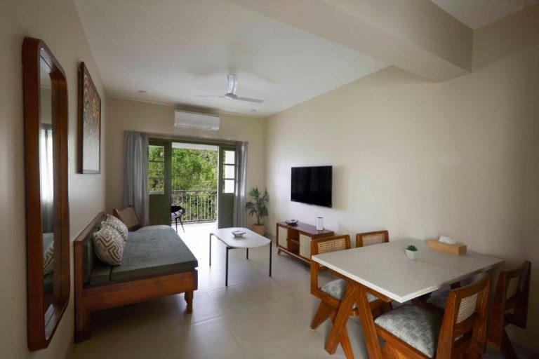 Salón comedor con sofá de madera, mesa de comedor y televisión en Radha House Siolim Boutique Hotel