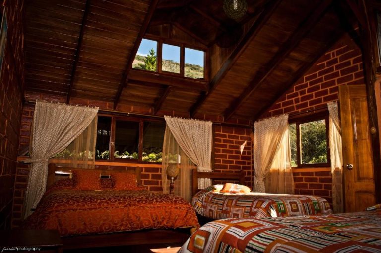 Habitación rústica con dos camas y techo de madera en cabaña de ladrillo del Hotel La Casta