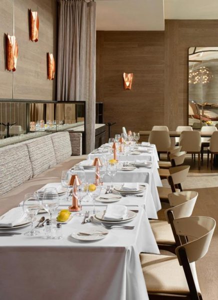 Restaurante elegante del Debaines Hotel Santiago con mesas blancas, copas de cristal y decoración en tonos cobre