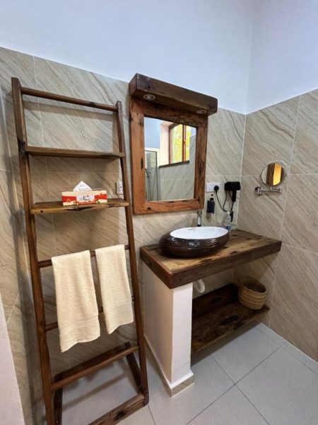 Baño rústico con lavabo artesanal y estantería de madera en M&M Villas Zanzibar
