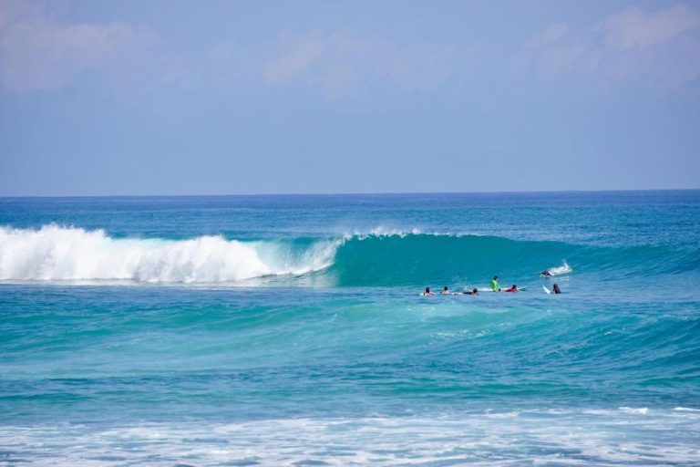 Surfistas esperando olas perfectas en el mar turquesa frente al La Curadiña Encuentro Surf Hotel