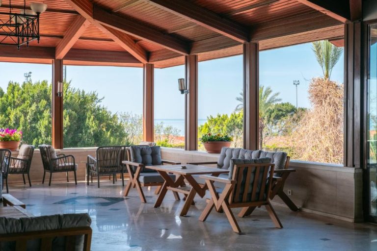 Terraza cubierta con mesas y sillones de madera con vistas al mar en Belconti Resort Hotel