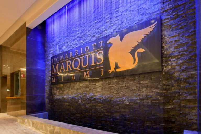 Lobby del JW Marriott Marquis Miami con muro de piedra iluminado y logo del hotel