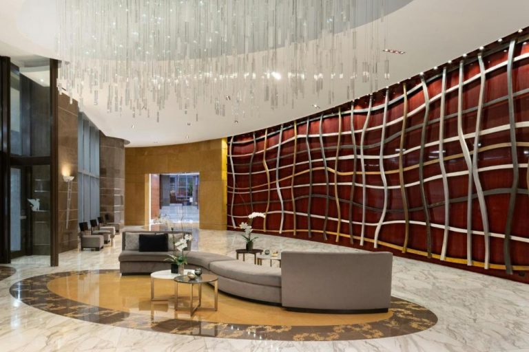 Lujoso lobby del JW Marriott Marquis Miami con sofás curvos, lámpara de cristal y mural decorativo en rojo