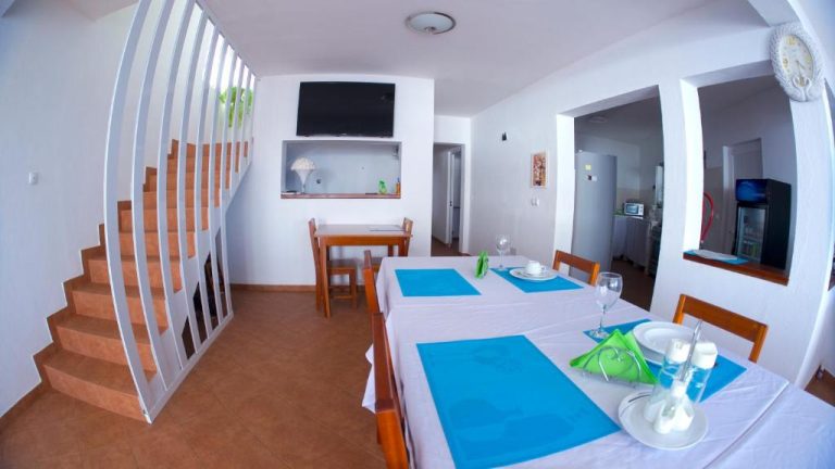 Comedor interior con mesas blancas y manteles azules junto a escalera en Cacimba Sunset Lodge