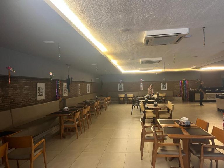 Amplio salón comedor del Flat Ramad con mesas de madera, sillas y aire acondicionado central