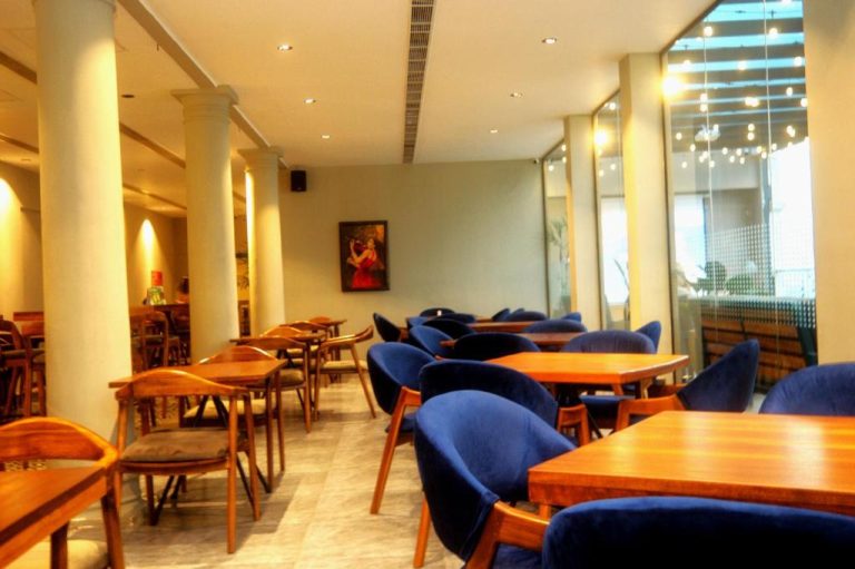 Elegante salón comedor del Fairway Colombo con sillas azules y mesas de madera en Sri Lanka