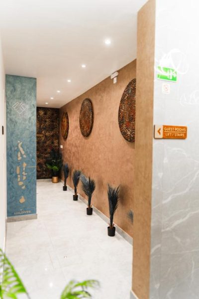 Pasillo decorado con arte maldivo y plantas en el Aina Residency Beachfront Hotel