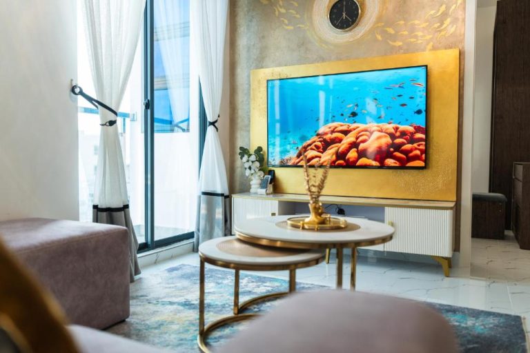 Salón de lujo con televisor en panel dorado y mesas de centro en Aina Residency Beachfront Hotel
