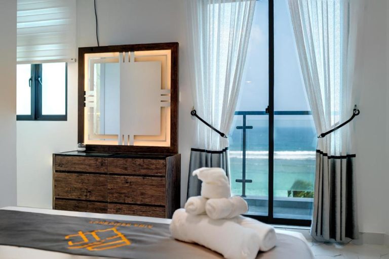 Habitación con vestidor iluminado y balcón con vistas al mar en Aina Residency Beachfront Hotel