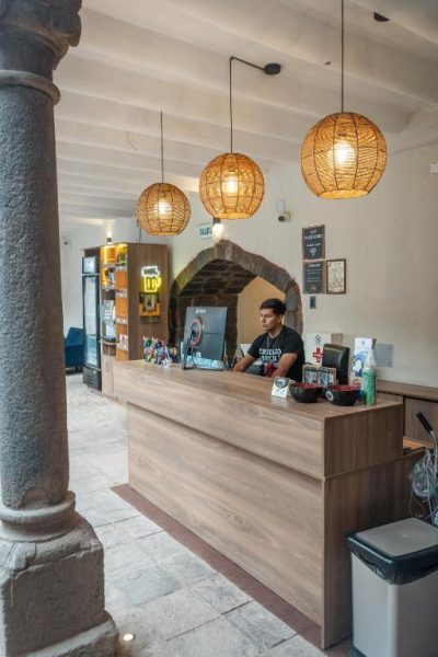 Recepción principal del Way Kap Hostel Cusco con mostrador de madera e iluminación cálida de mimbre