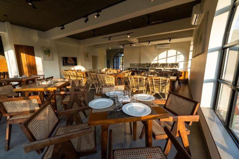 Restaurante interior del SinQ Anvaya con mesas de madera y sillas de ratán en un ambiente cálido y luminoso