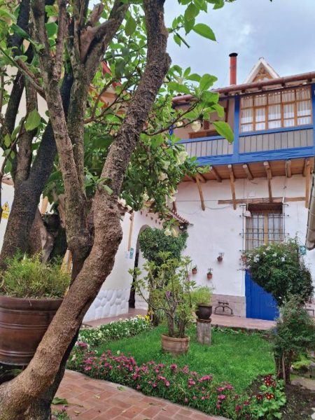 Jardín exterior con flores y árboles frondosos en la Casona La Recoleta, edificio colonial con balcón azul