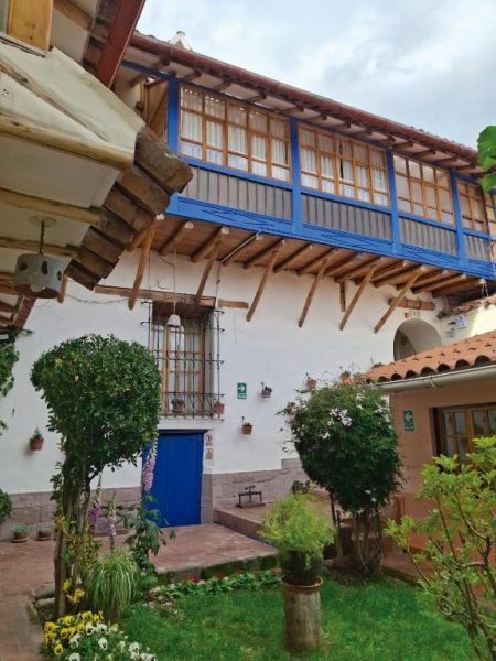 Patio interior con jardín y balcón colonial de madera azul en Casona La Recoleta, Cusco
