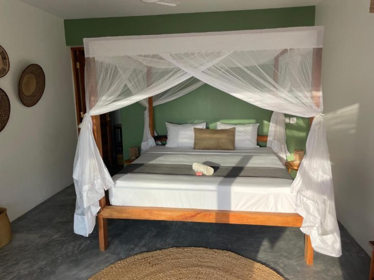 Habitación con cama de madera y dosel con mosquitera blanca en Palmera Zanzibar Eco Boutique Hotel