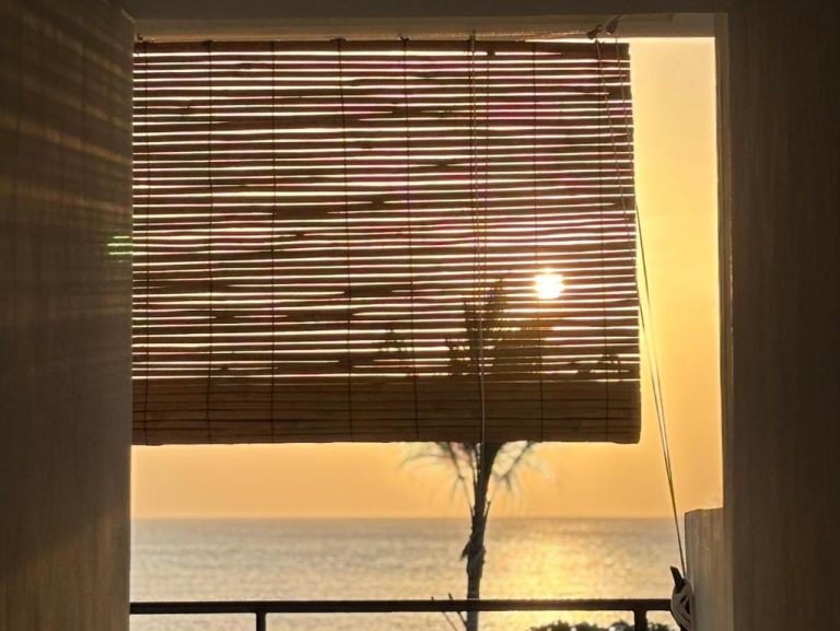 Vista al mar al atardecer desde habitación con persiana de bambú en Palmera Zanzibar Eco Boutique Hotel