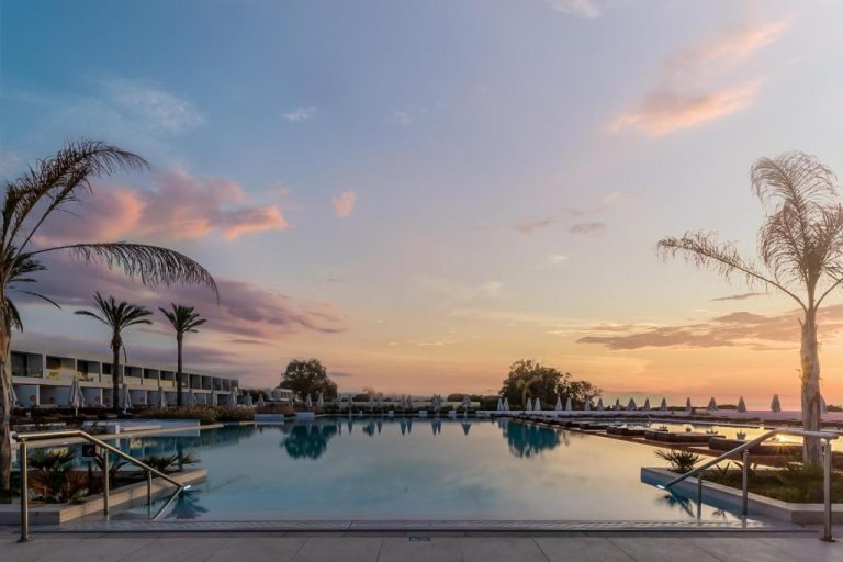 Piscina exterior al atardecer con palmeras y vistas al mar en Gennadi Grand Resort Premium All Inclusive
