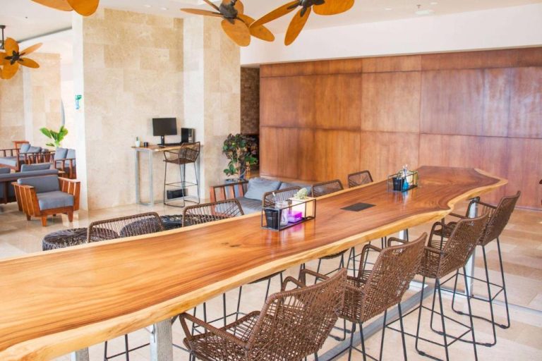 Barra de madera natural en el lobby del Wyndham Tamarindo con sillas de mimbre y ventiladores de techo
