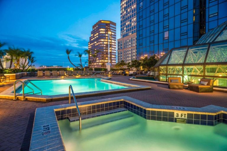 Piscina exterior iluminada de noche con jacuzzi en el Hilton Tampa Downtown con vistas al skyline