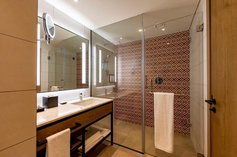 Baño moderno con ducha de azulejos rojos y lavabo iluminado en Hyatt Place Nairobi Westlands
