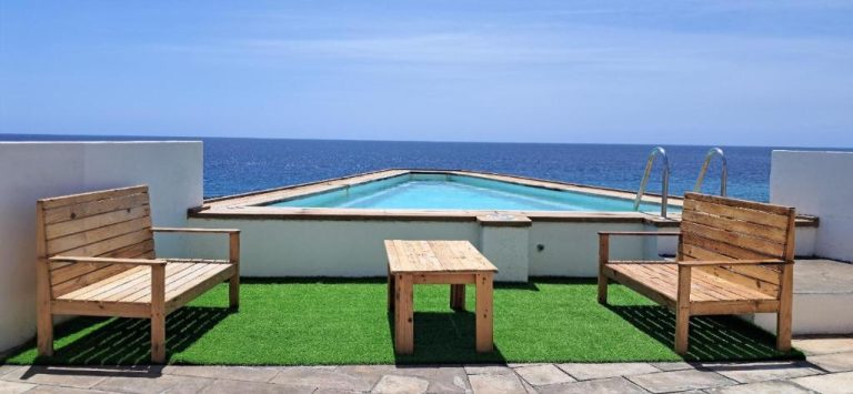 Piscina exterior con vistas al océano y terraza con sillas de madera en Cacimba Sunset Lodge