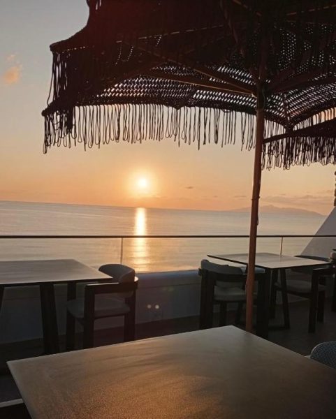 Terraza del Hotel Aelia Thalassa con mesas y sombrilla al atardecer frente al mar en Grecia