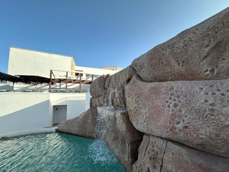 Cascada artificial sobre rocas volcánicas en la piscina exterior del hotel Aelia Thalassa