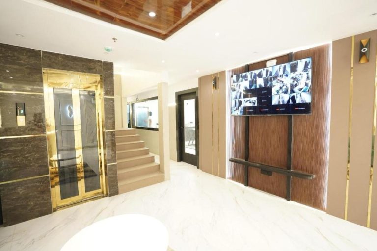 Lobby de mármol blanco con ascensor dorado y pantallas de seguridad CCTV en el Hotel Lancaster
