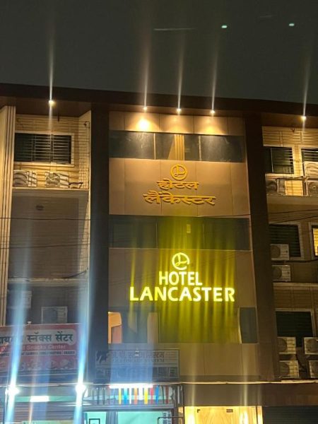 Fachada nocturna iluminada del Hotel Lancaster con letrero en hindi y letras doradas