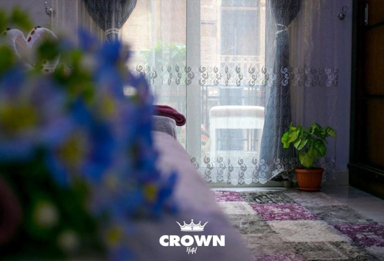 Habitación del Crown Home Hotel con ventana, cortinas de encaje y planta decorativa interior