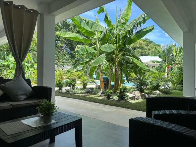 Terraza con sofás y vistas al jardín tropical con palmeras y piscina del Hotel Good Life