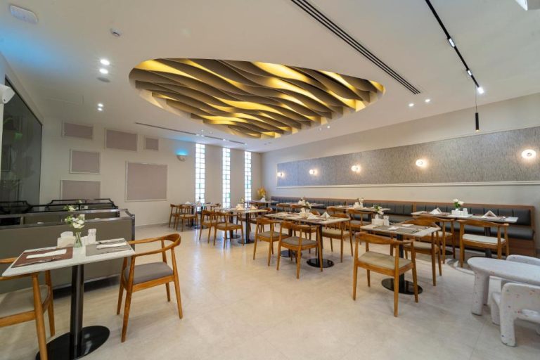 Restaurante moderno del Hill Top Hotel con techo ondulado dorado, mesas de madera y elegante decoración interior