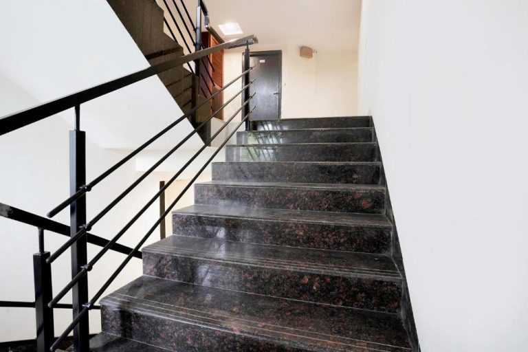 Escaleras de mármol oscuro con barandilla metálica negra en FabHotel Kamran Residency cerca de LBS Marg
