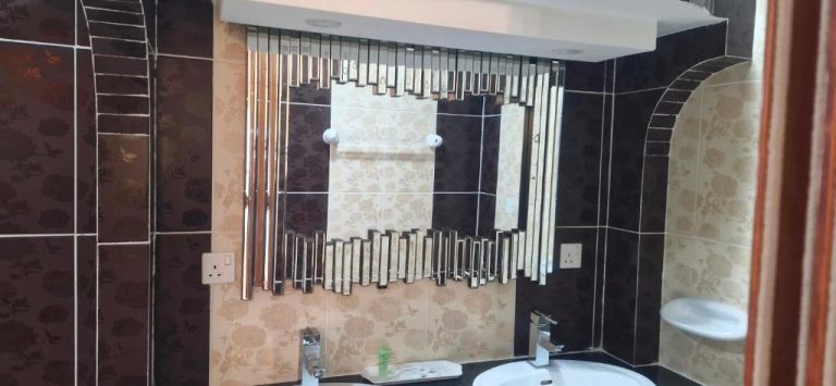 Baño moderno con espejo decorativo y lavabo del Riyam Hotel, con azulejos en tonos oscuros y beige