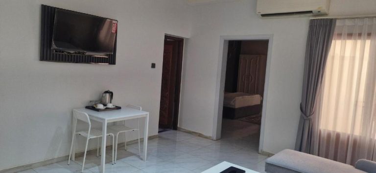 Sala de estar con televisión y acceso al dormitorio en Riyam Hotel, decoración moderna y luminosa