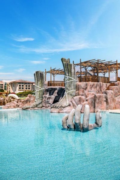 Piscina exterior con escultura de rocas y dedos gigantes en el hotel Regnum The Crown