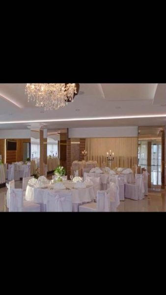 Salón de banquetes elegante con mesas vestidas en blanco y lámpara de araña en Levant Residence