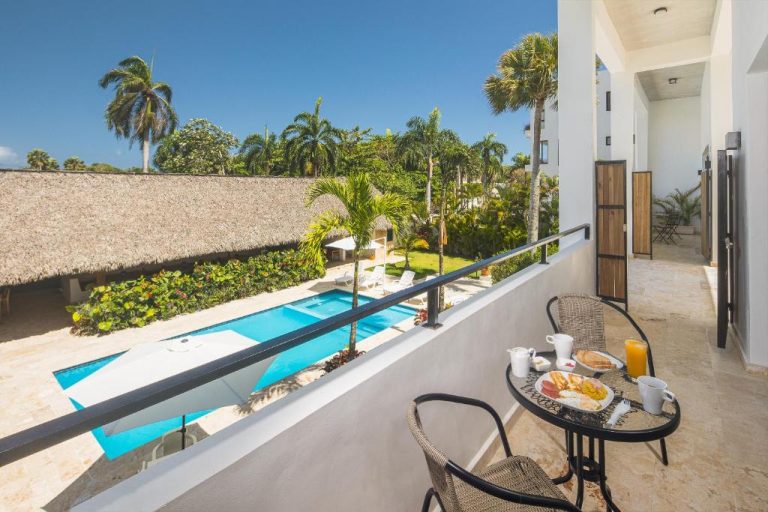 Terraza con desayuno y vistas a la piscina exterior rodeada de palmeras en La Curadiña Encuentro Surf Hotel