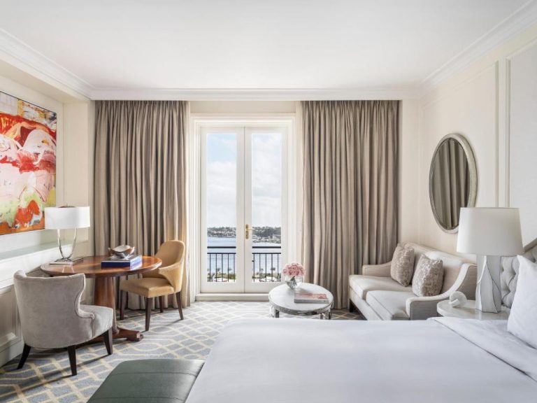 Habitación deluxe con vista al puerto y balcón en The Langham Sydney, decoración elegante en tonos neutros