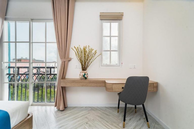Escritorio de madera con silla y balcón en habitación del Novus Sol Hotel & Apartment Sunset Town Phu Quoc