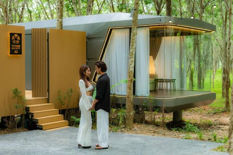 Pareja frente a cabana de lujo con paredes de cristal rodeada de bosque en Timber Society Boutique Hideaway