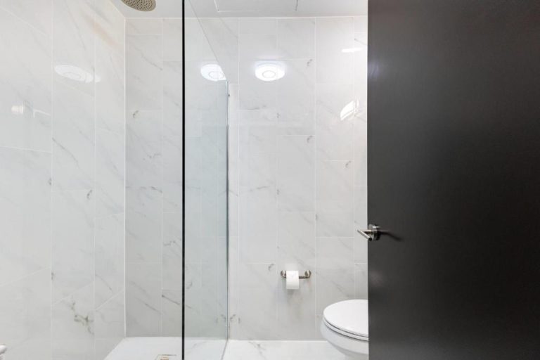 Baño moderno con ducha de cristal y revestimiento de mármol blanco en Hotel Milano