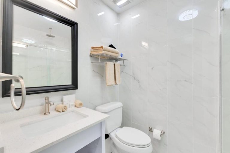 Baño moderno con revestimiento de mármol blanco, ducha y lavabo del Hotel Milano