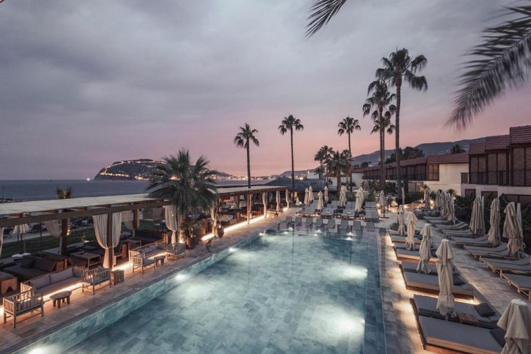 Piscina exterior iluminada al atardecer con tumbonas y palmeras en Day One Beach Resort & SPA Adult Only