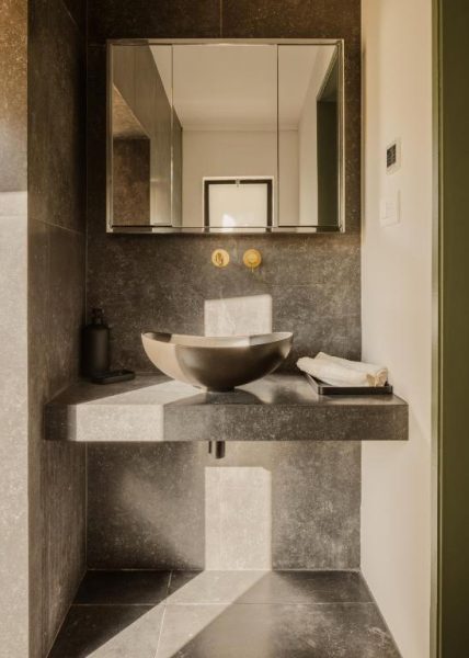 Baño moderno con lavabo de diseño sobre encimera de piedra y grifo dorado en Hotel Aritis 3